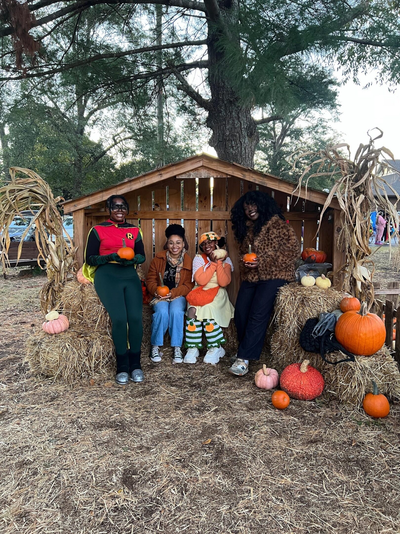 Four people in colorful costumes posing by a wooden cabin with Halloween decorations.