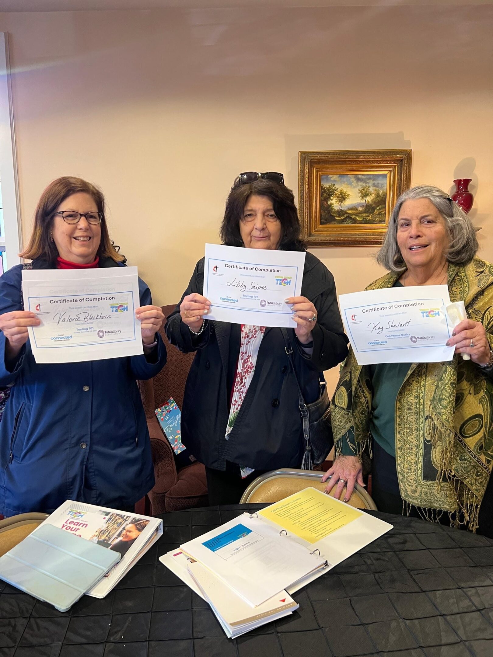 Three women proudly holding certificates indoors.