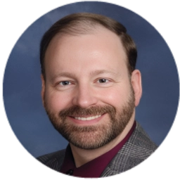 Smiling man with a beard and suit against a blue background.