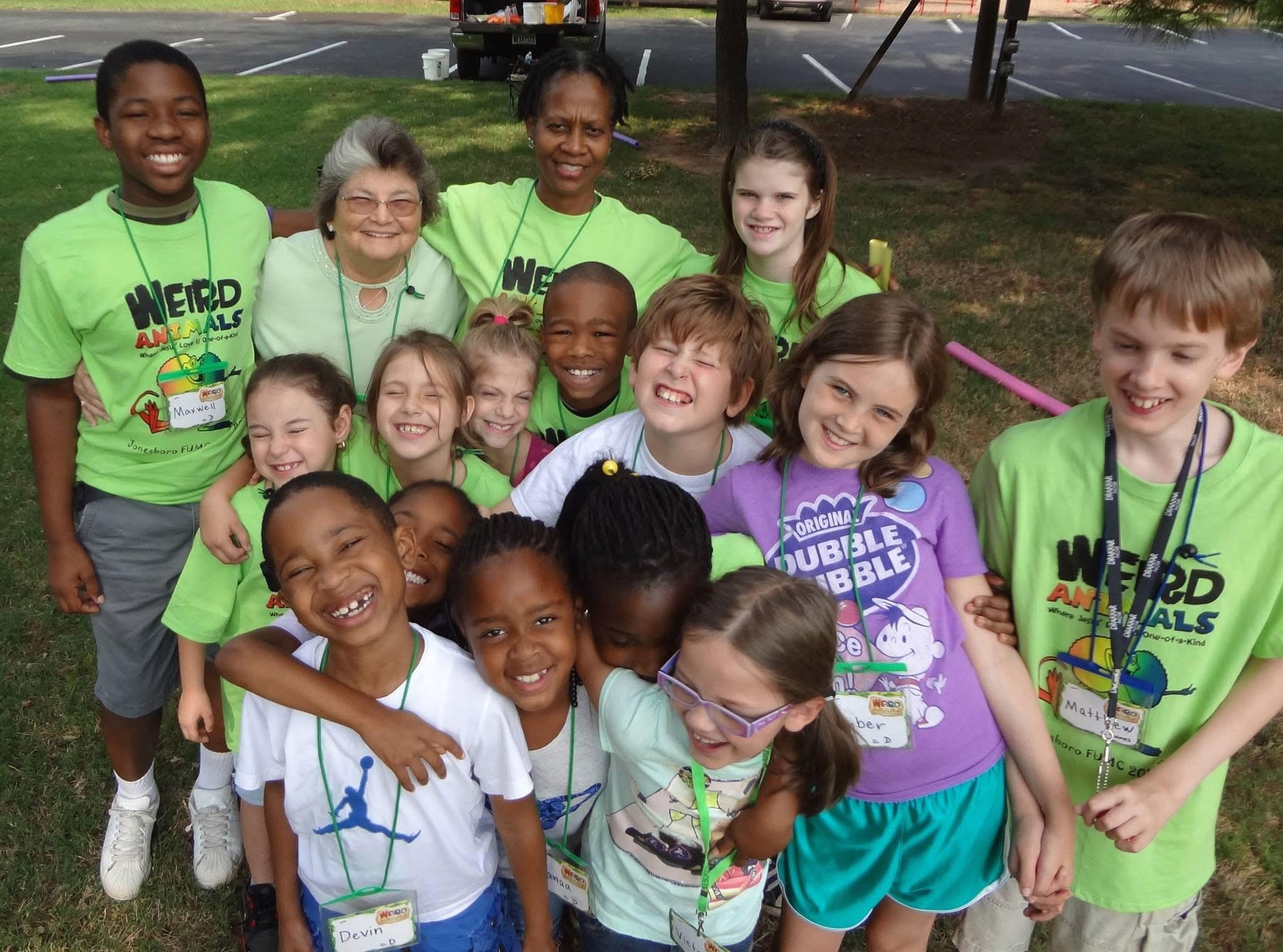 A joyful group of children and two adults posing outdoors in colorful t-shirts.