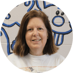 Smiling woman with shoulder-length brown hair in front of a blue mural.