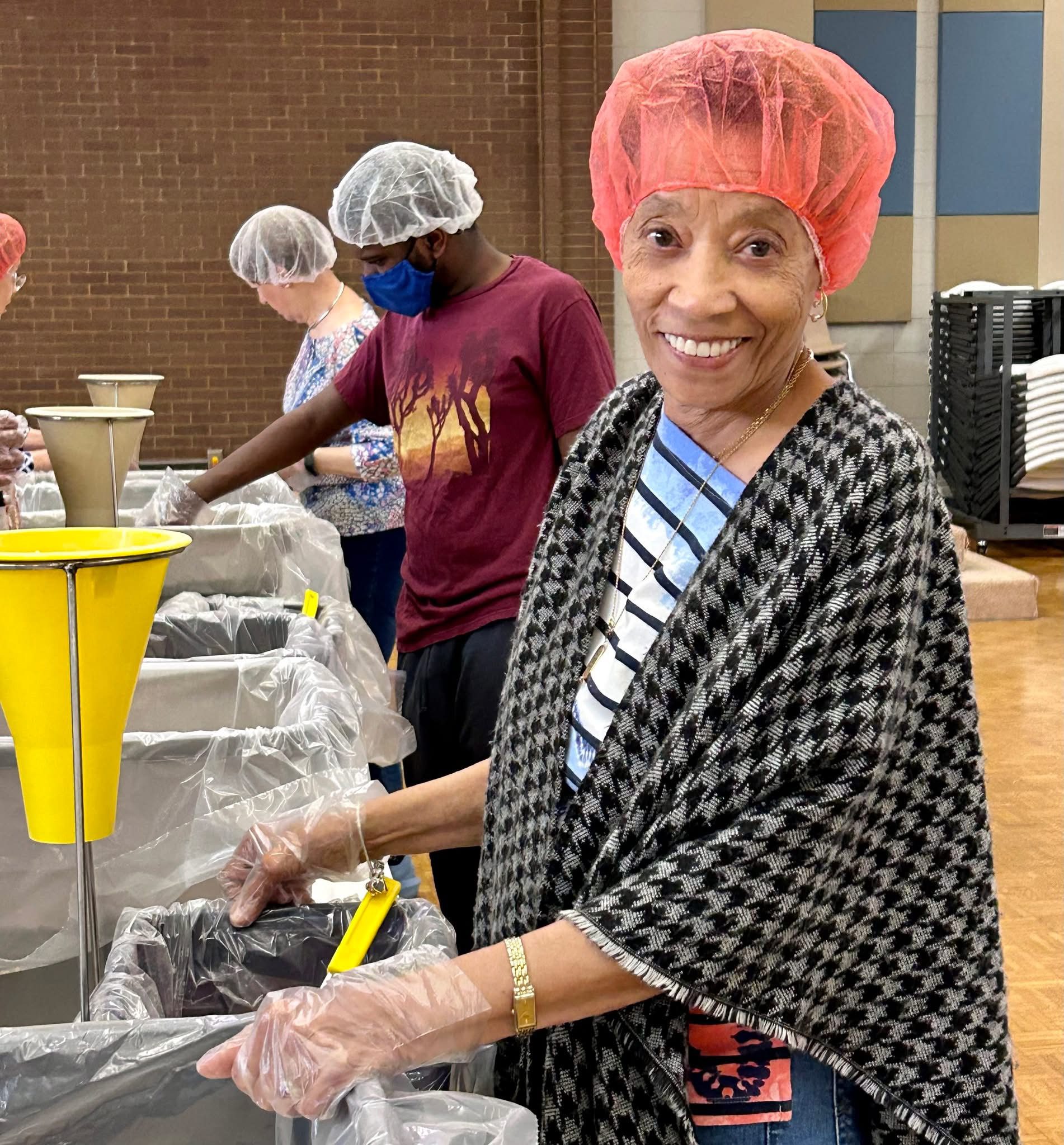 Smiling woman volunteers with food packing at a community event.