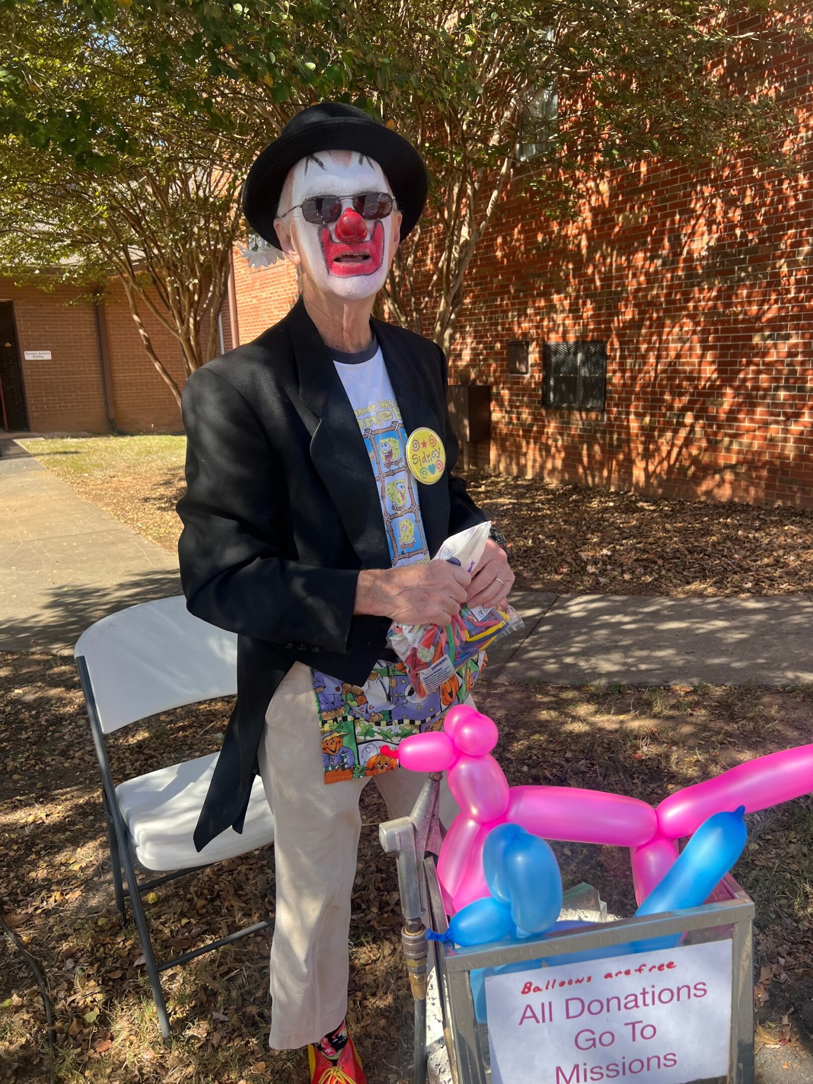A person in clown makeup holding balloons outdoors.