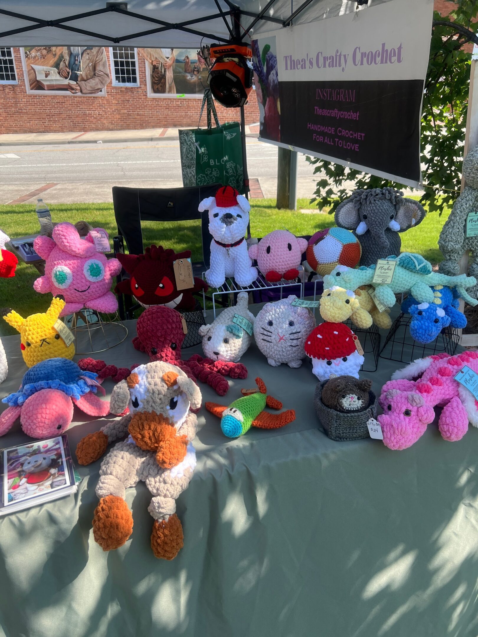 Table displaying colorful handmade stuffed animals at an outdoor market.