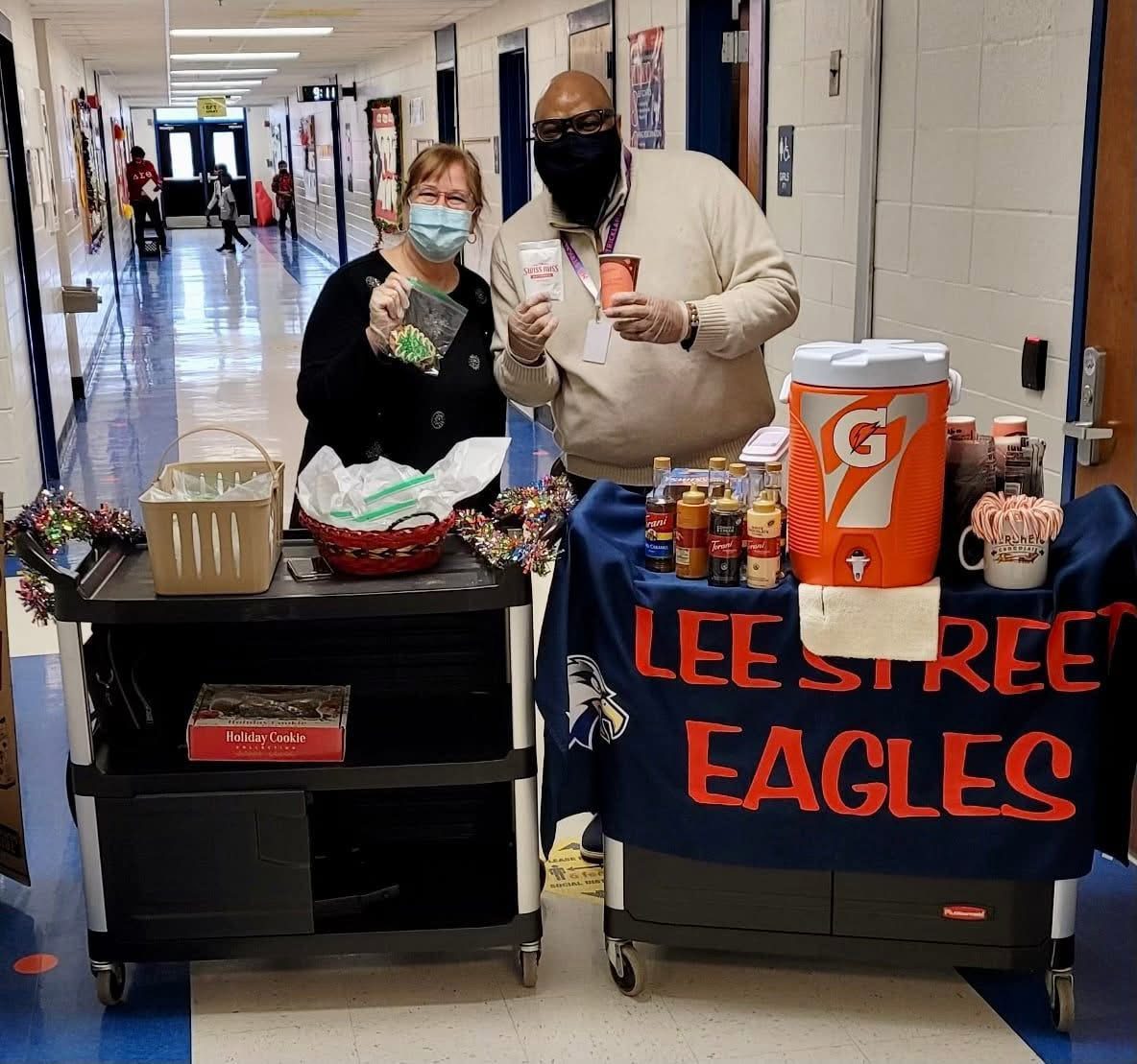 Two masked individuals with donation carts in a school hallway.